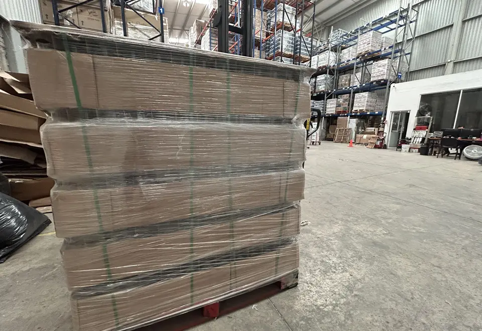 Tarima de cajas de cartón emplayada y flejada en la nave de Mubit Logística, con racks de tarimas al fondo