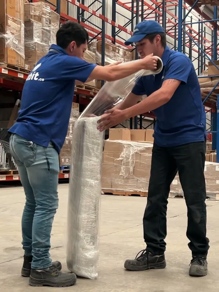 Dos operadores de Mubit con uniforme azul manejando un rollo de película emplayable